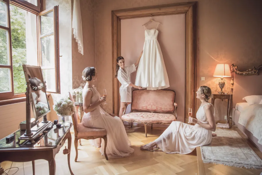 Braut mit ihren Brautjungfern beim Getting Ready in einem Zimmer des Schlosses, das Brautkleid hängt an der Wand